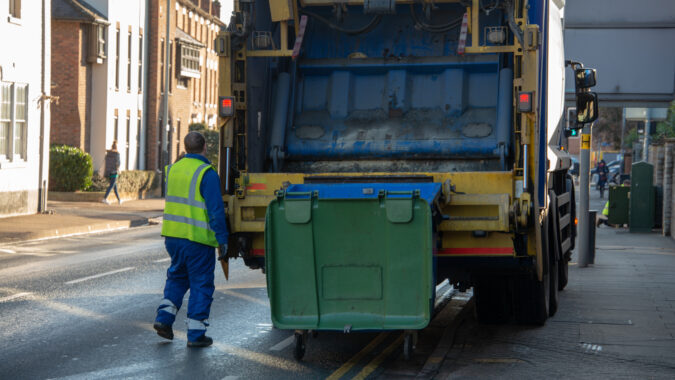 bin lorry or waste truck collects refuse from a green dumpster