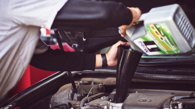 man pouring oil into car engine.