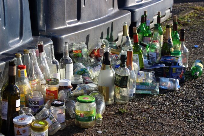 glass bottles and jars on the ground in front of recycling bins.